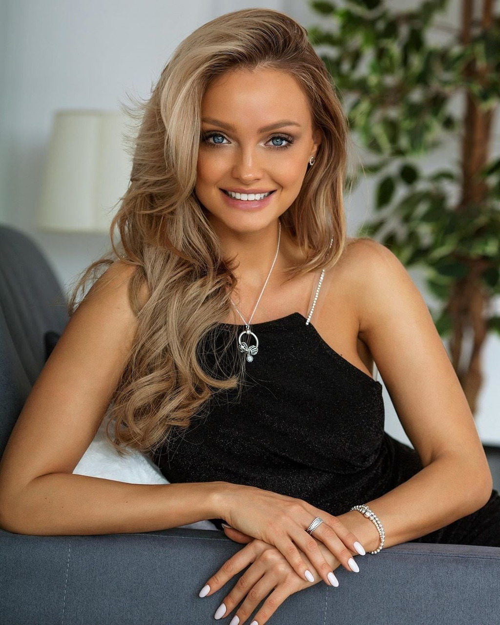 Smiling woman with wavy blonde hair wearing black dress in indoor portrait
