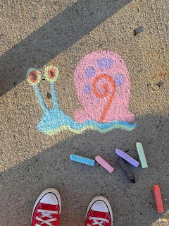 Colorful chalk drawing of Gary the snail on a sidewalk with chalk pieces and red Converse shoes