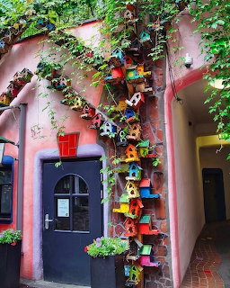 Colorful birdhouses mounted on pink wall with green ivy and flower pots