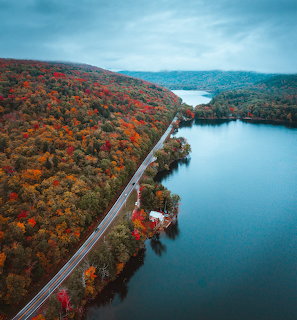 Aerial view of a road alongside a river surrounded by colorful fall trees and hills