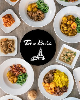 Overhead view of several plated meals around a black circle reading Toko Bali on a wooden table