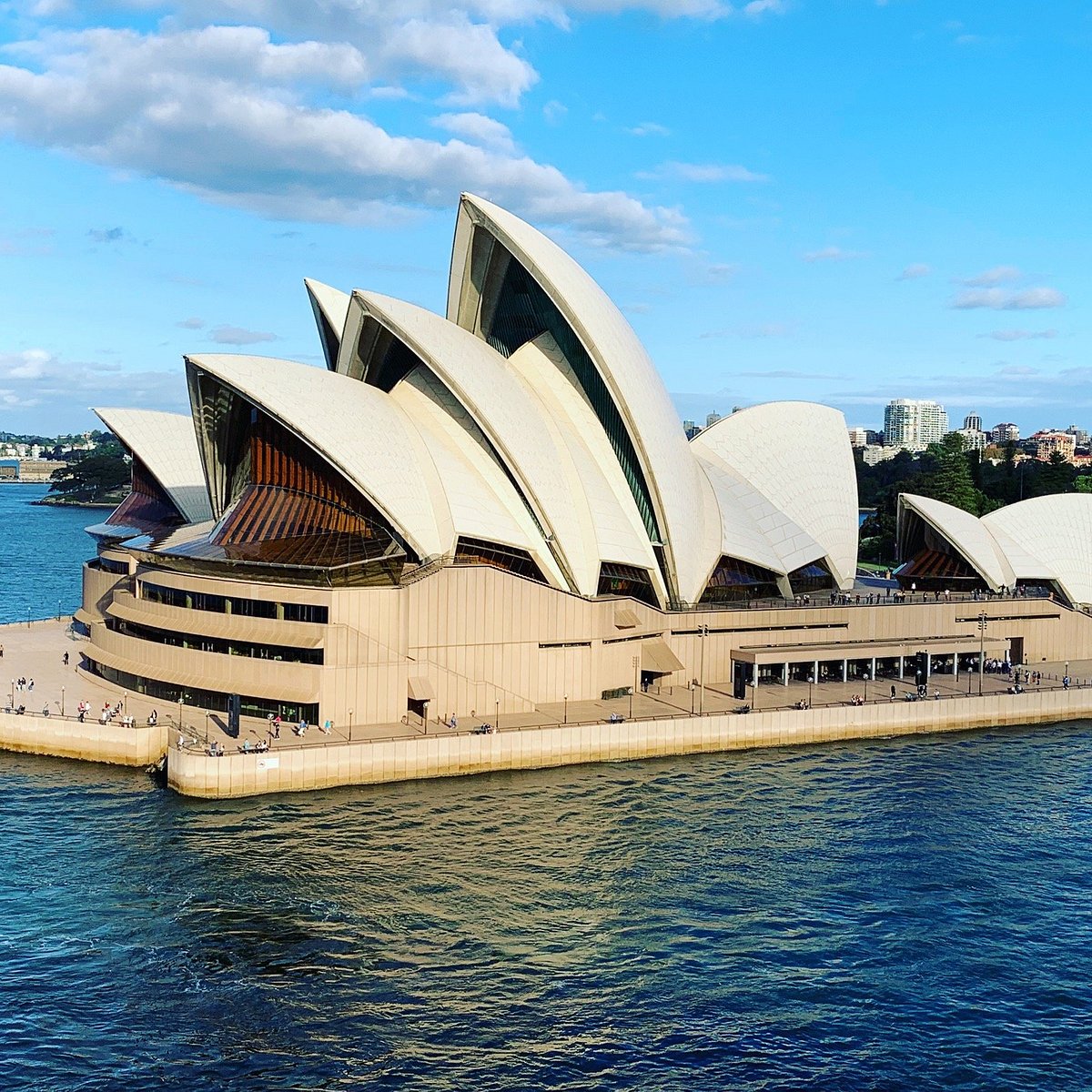 Sydney Opera House with white sail-like roof against blue sky and harbor water
