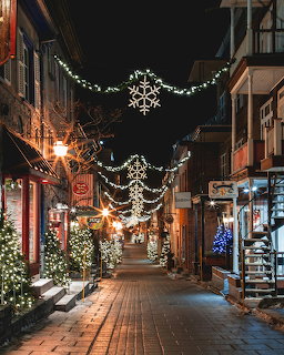 Night view of a brick street decorated with illuminated snowflake lights and Christmas trees lining storefronts