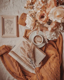 Cozy flatlay with book, coffee, cream flowers and a mustard knit blanket on bedding