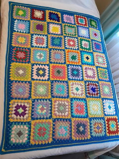 Colorful crochet blanket with multicolored granny square pattern laid on white surface