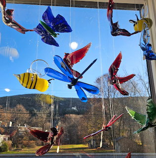 Hanging glass art mobile with colorful insects including butterflies, dragonflies, and a bee against a window
