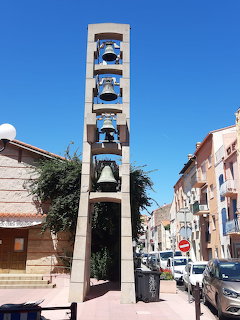 Modern bell tower on a sunny street with pastel buildings and parked cars