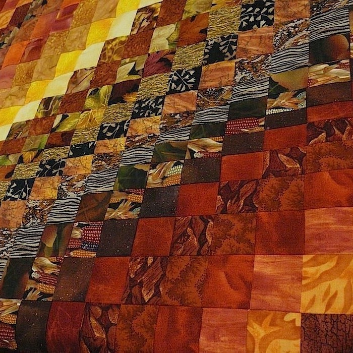 Diagonal view of a patchwork quilt with squares in warm autumn colors and varied patterns