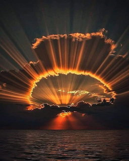 Dramatic sunset over ocean with golden sun rays radiating through dark clouds
