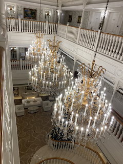Two crystal chandeliers in a grand white atrium with balcony railings and seating below