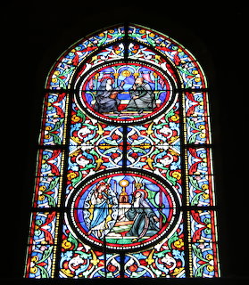 Gothic stained glass cathedral window with religious scenes in circular panels surrounded by colorful floral ornamental borders