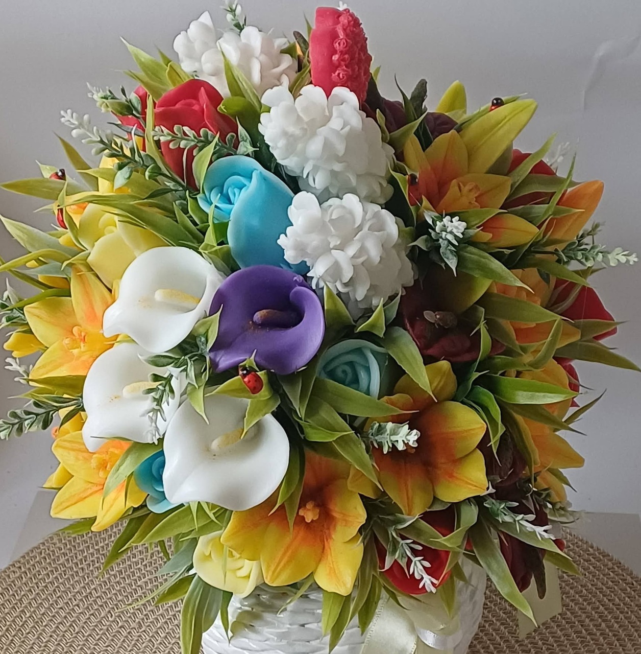 Colorful artificial flower bouquet with mixed blooms in white vase on beige surface