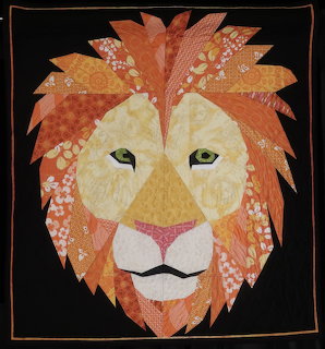 Textile art depicting a lion's face with orange patterned fabric mane on black background