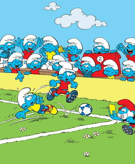 Cartoon Smurfs playing soccer on a green field with blue Smurf spectators in the background