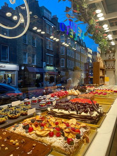 Bakery window filled with colorful cakes and pastries with London street reflection at twilight