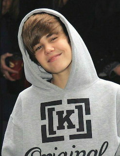 Justin Bieber smiling in a gray hoodie against a dark background