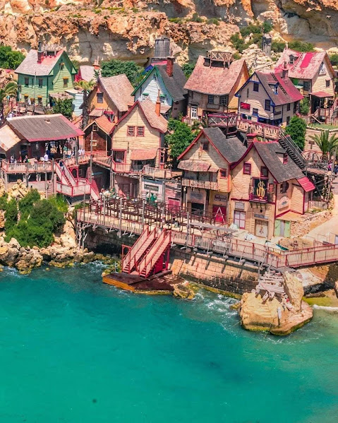 Aerial view of colorful wooden houses at Popeye Village Malta by turquoise water