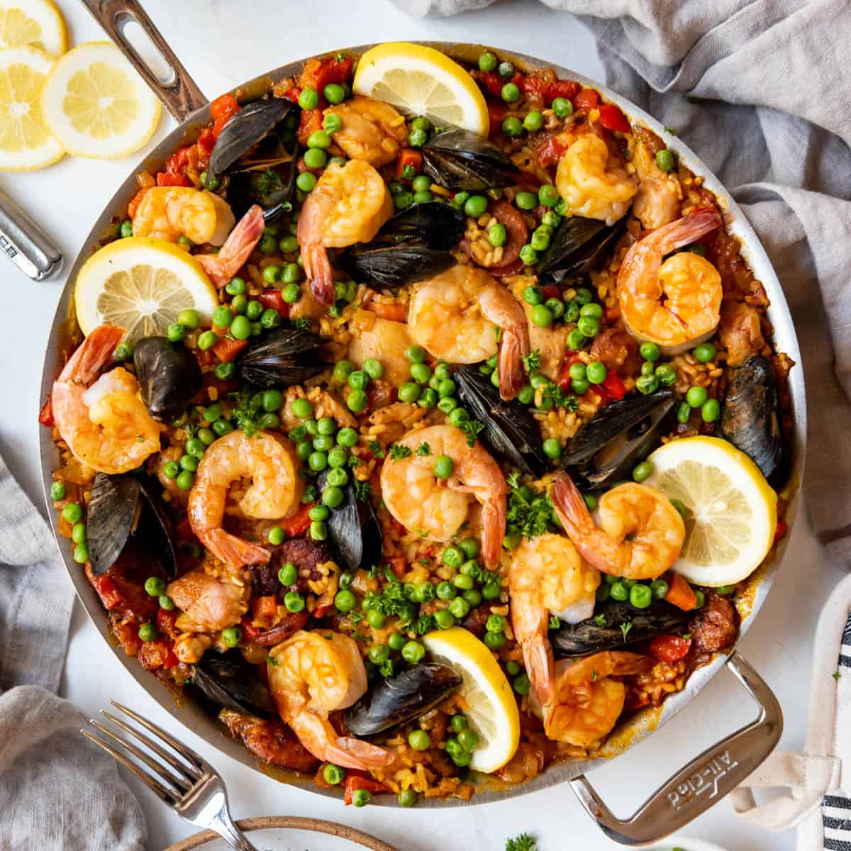 Top-down view of seafood paella with shrimp, mussels, peas, and lemon slices in a pan