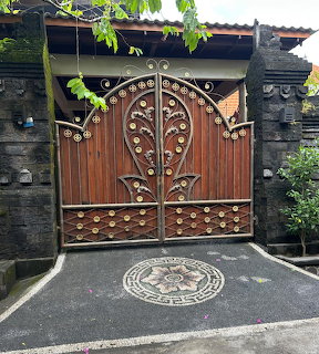 Ornate wooden double gate with iron scrollwork and circular metal decorations in a Balinese stone wall