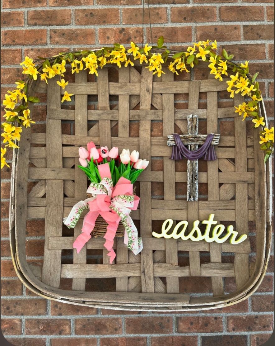 Woven basket wreath with yellow flowers, pink tulips bouquet, wooden cross, and Easter sign on brick wall