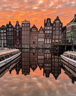 Row of historic Amsterdam canal houses with reflections in water at sunset