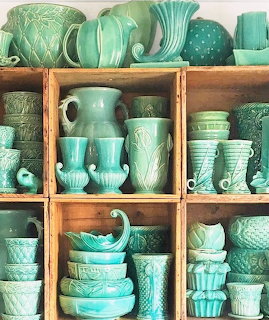 Wooden shelf displaying a large collection of vintage green McCoy pottery vases, pitchers, and bowls