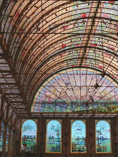Ornate arched ceiling with stained glass panels and geometric wooden framework above tall stained glass windows