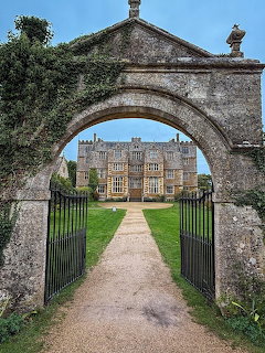 Stone archway framing view of historic manor house with formal gardens and gravel path