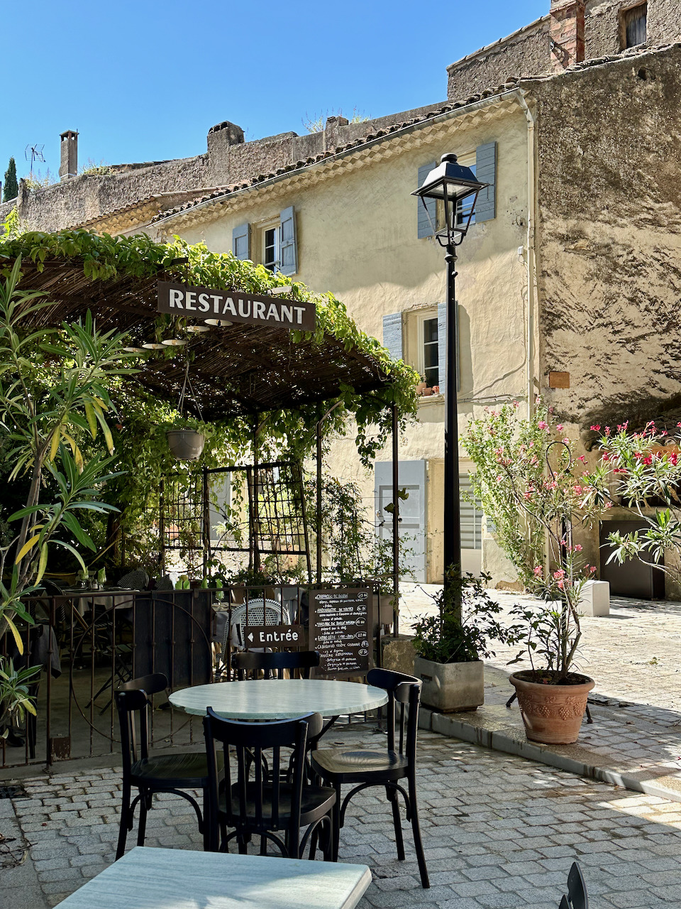 Outdoor café terrace in Cucuron, France, with bistro chairs, a street lamp, and a stone building restaurant