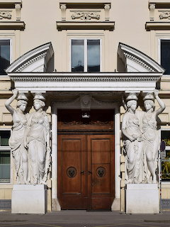 Neoclassical building entrance with caryatid columns and ornate wooden double doors in Vienna