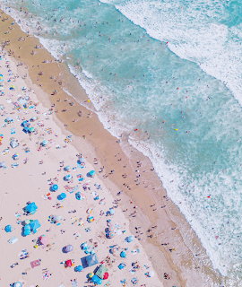 Aerial view of crowded beach with people on sand and turquoise ocean waves