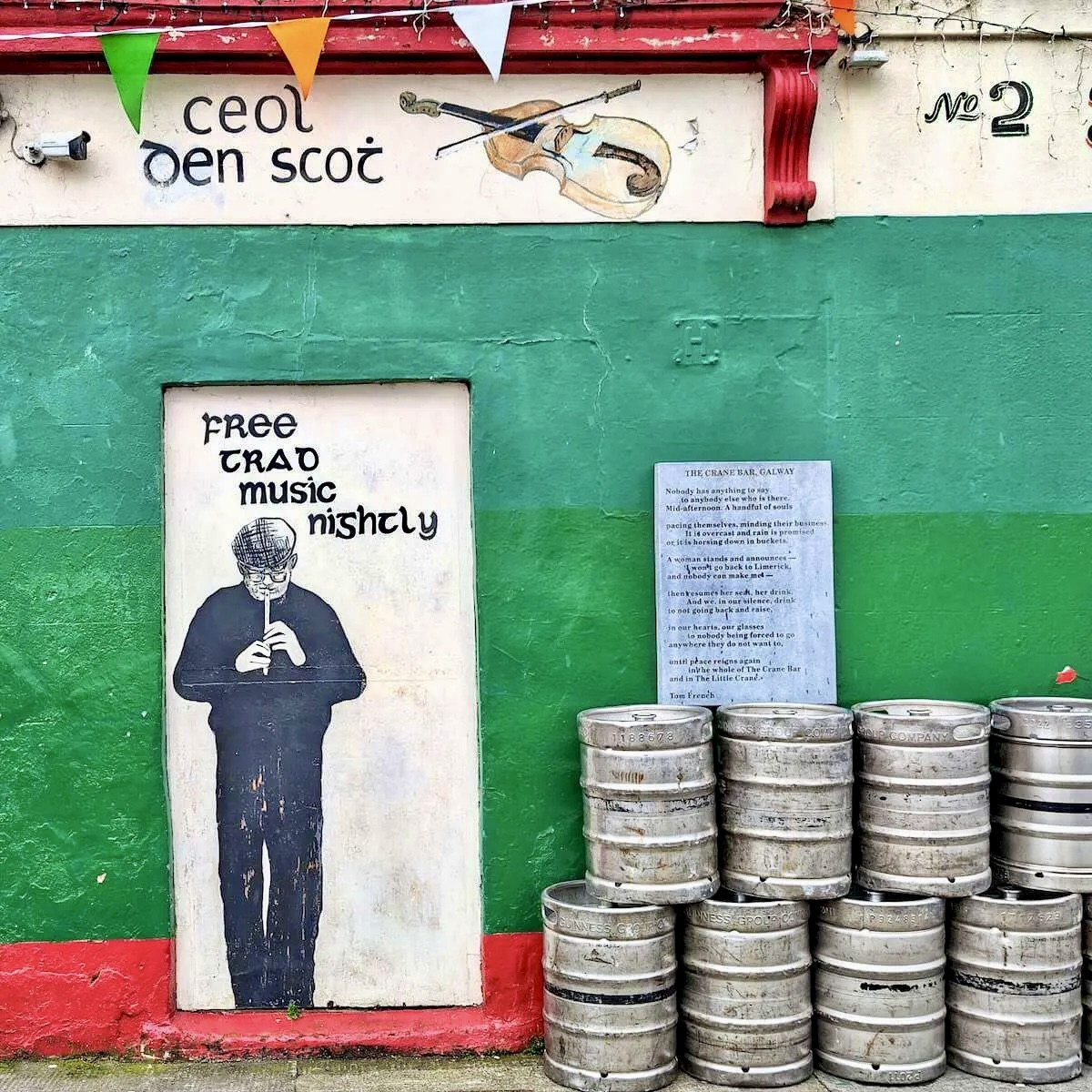 Irish pub exterior with green wall, stacked metal beer kegs, and traditional music poster
