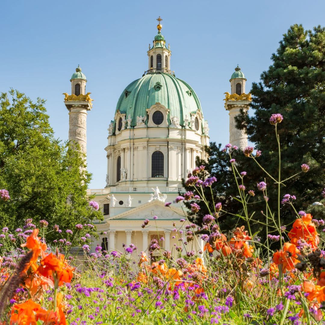 White domed church behind a colorful flower garden with trees and blue sky