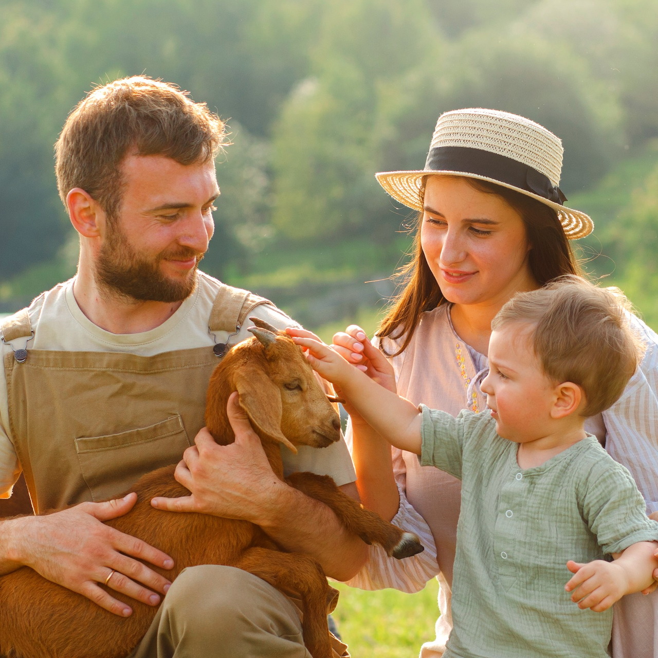 Man, woman, and child holding and petting a baby goat outdoors