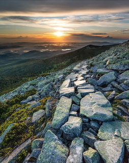 Rocky mountain slope at sunset with layered ridges and a cloudy glowing sky