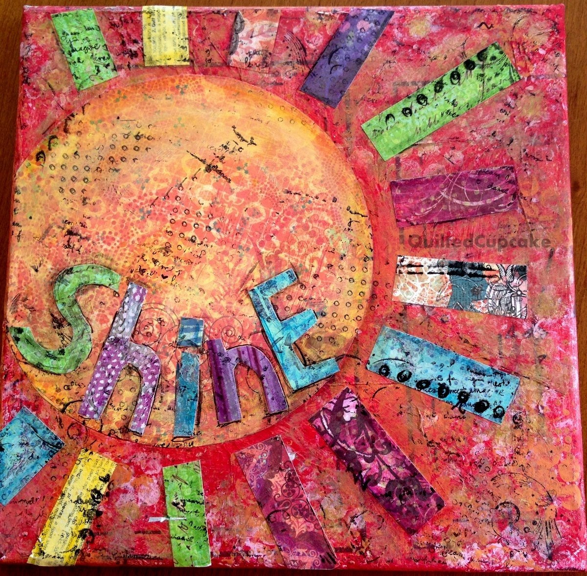 Mixed media collage with orange sun, colorful SHINE text, and patterned paper pieces on pink textured background