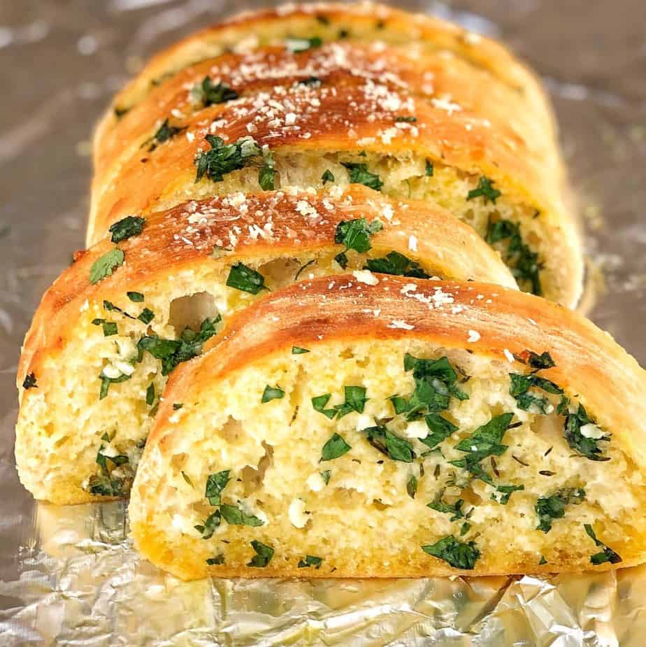 Sliced ciabatta garlic bread with herbs and sesame seeds on parchment paper