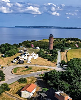 Aerial view of a tall brick lighthouse tower at Kap Arkona with surrounding buildings, green fields, and the Baltic Sea
