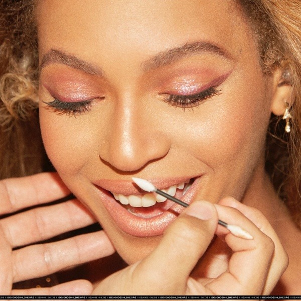 Close-up of a woman with glowing peach eyeshadow smiling while lip liner is applied to her lips