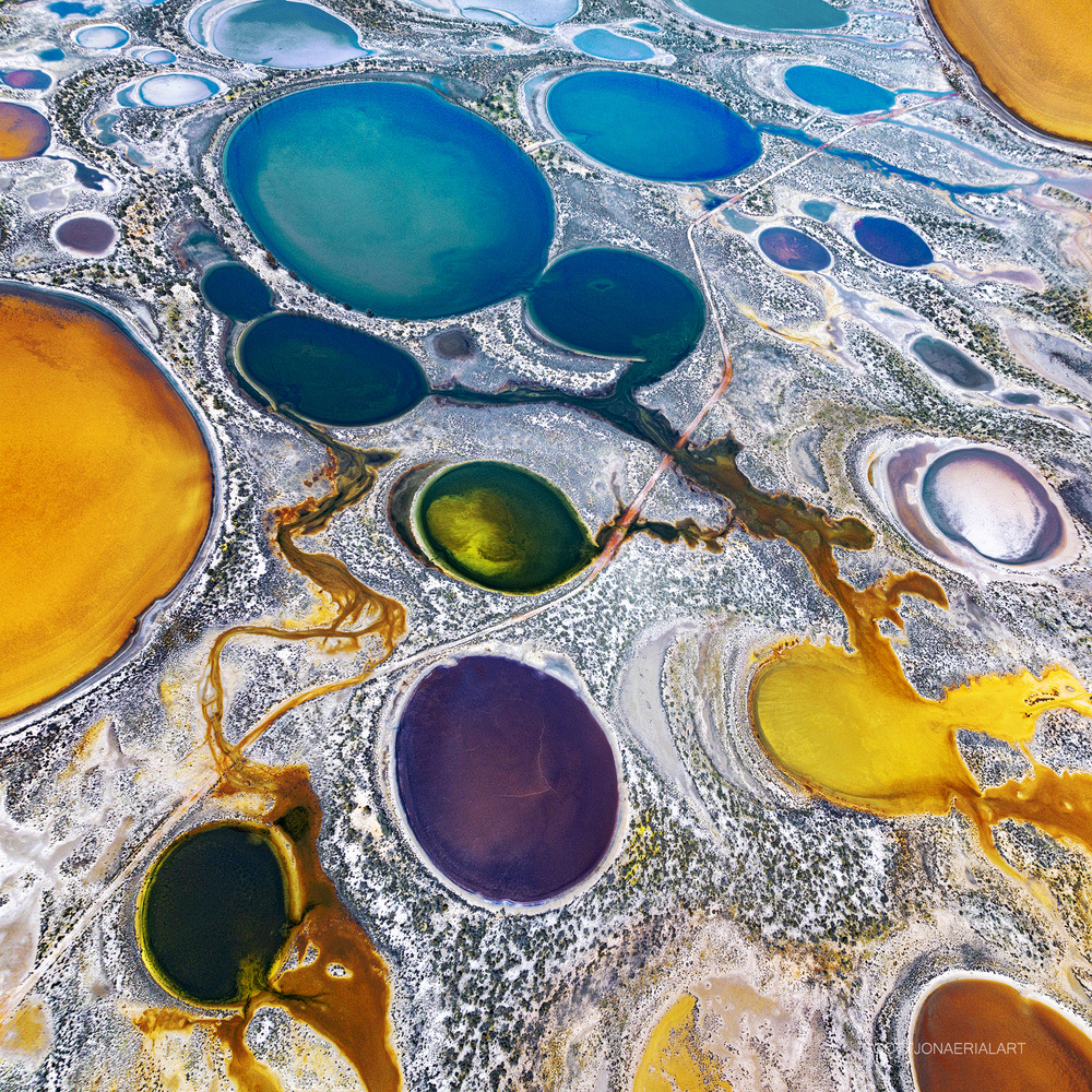 Aerial art showing colorful circular pools with bubbles and metallic borders in blue, yellow, purple, and green tones