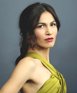 Woman with dark hair in a loose braid wearing a green halter dress posing against a gray background