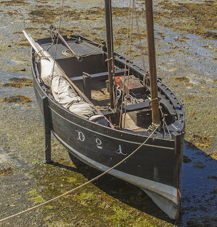 Black wooden sailboat beached on a muddy tidal flat at low tide