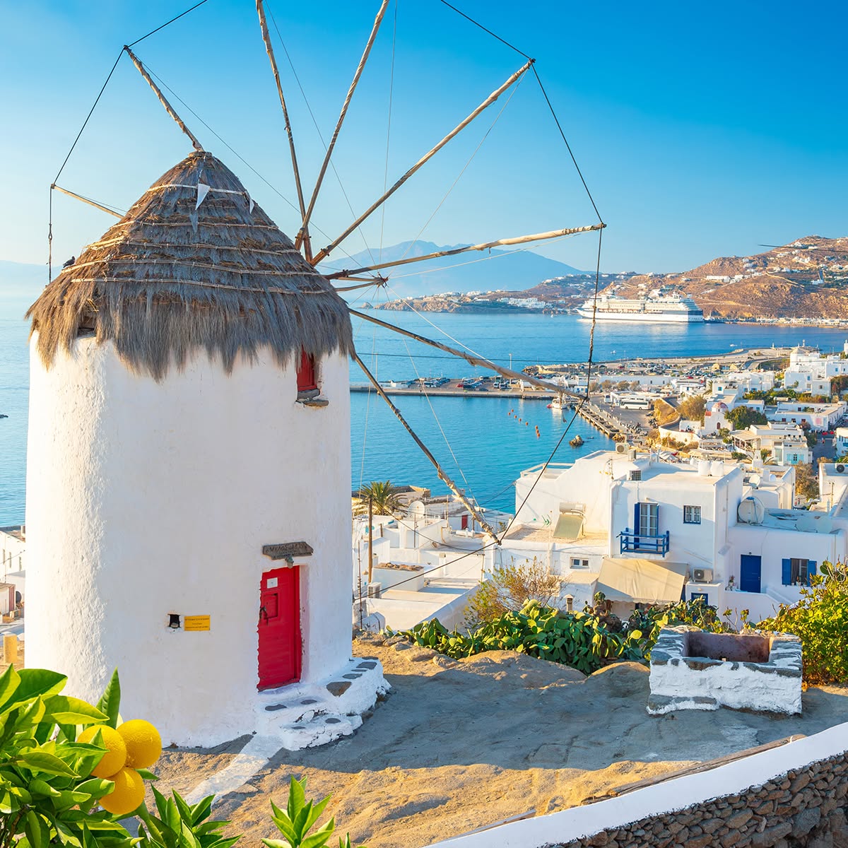 White windmill above a blue bay and hillside village on a sunny Greek island