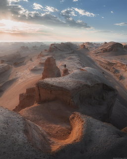Eroded desert rock formations in Dasht-e Lut with a person standing on a ridge at sunset