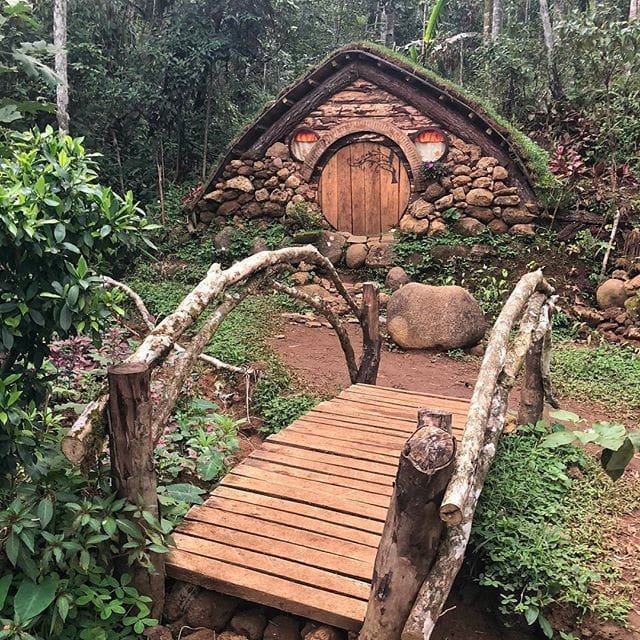 Small hobbit house with round door and wooden bridge in garden