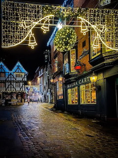 Cobblestone street in Lincoln at night with golden Christmas bell lights and Tudor buildings including Magna Carta shop