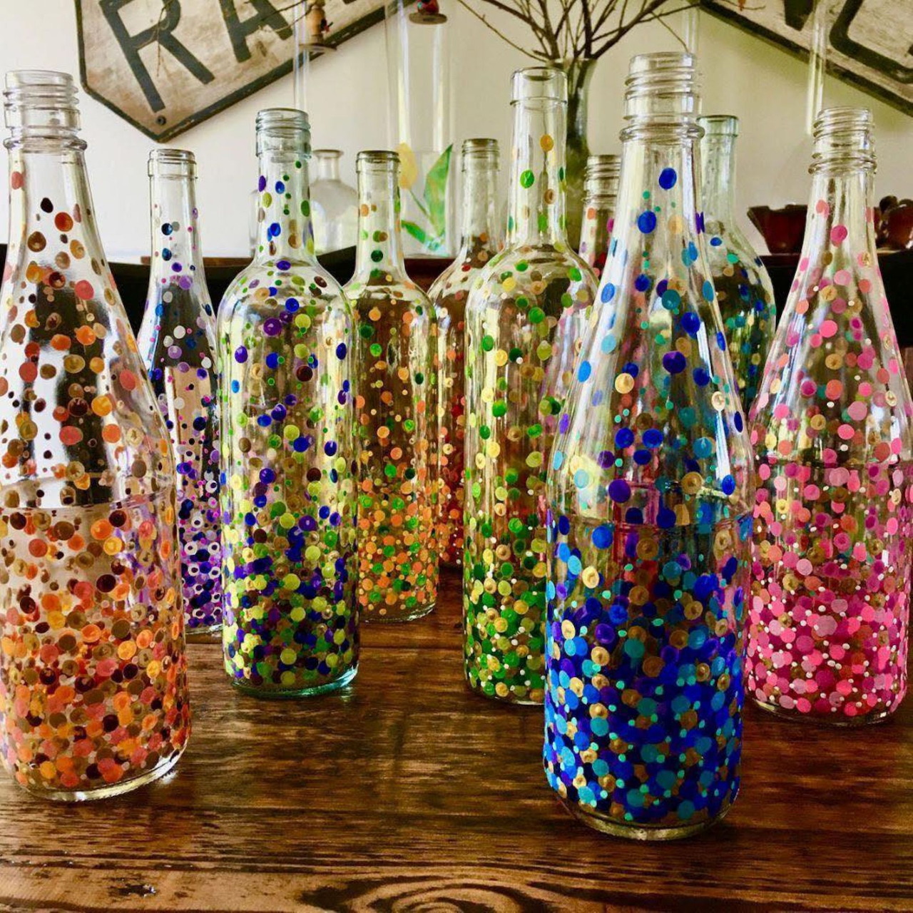 Row of glass bottles decorated with colorful painted dots in various rainbow patterns on wood table
