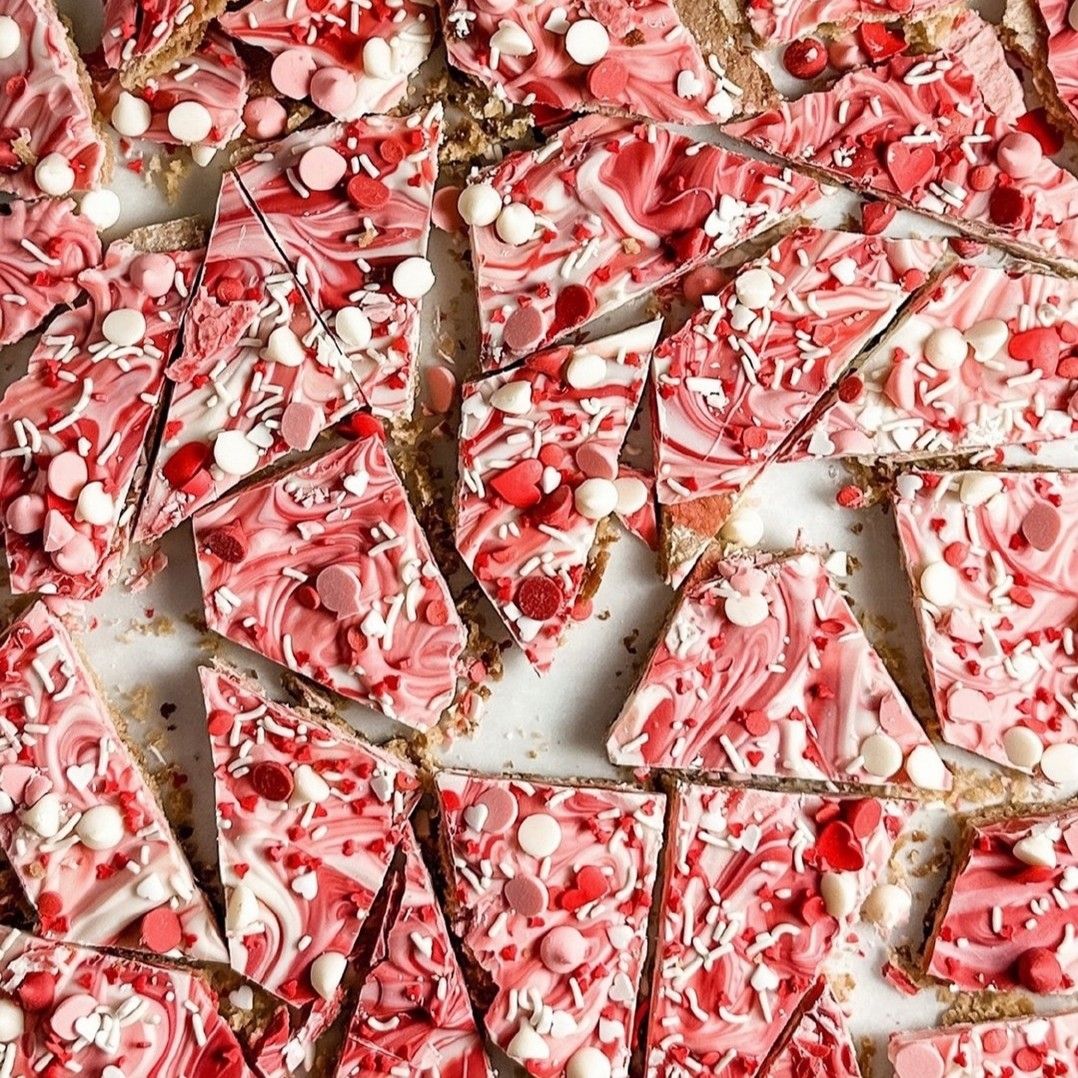 Pieces of pink and white chocolate bark with sprinkles and candy bits scattered on a light background