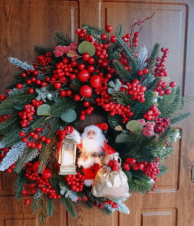 Christmas wreath with red berries, pine branches, pine cones, and Santa figurine on wood door