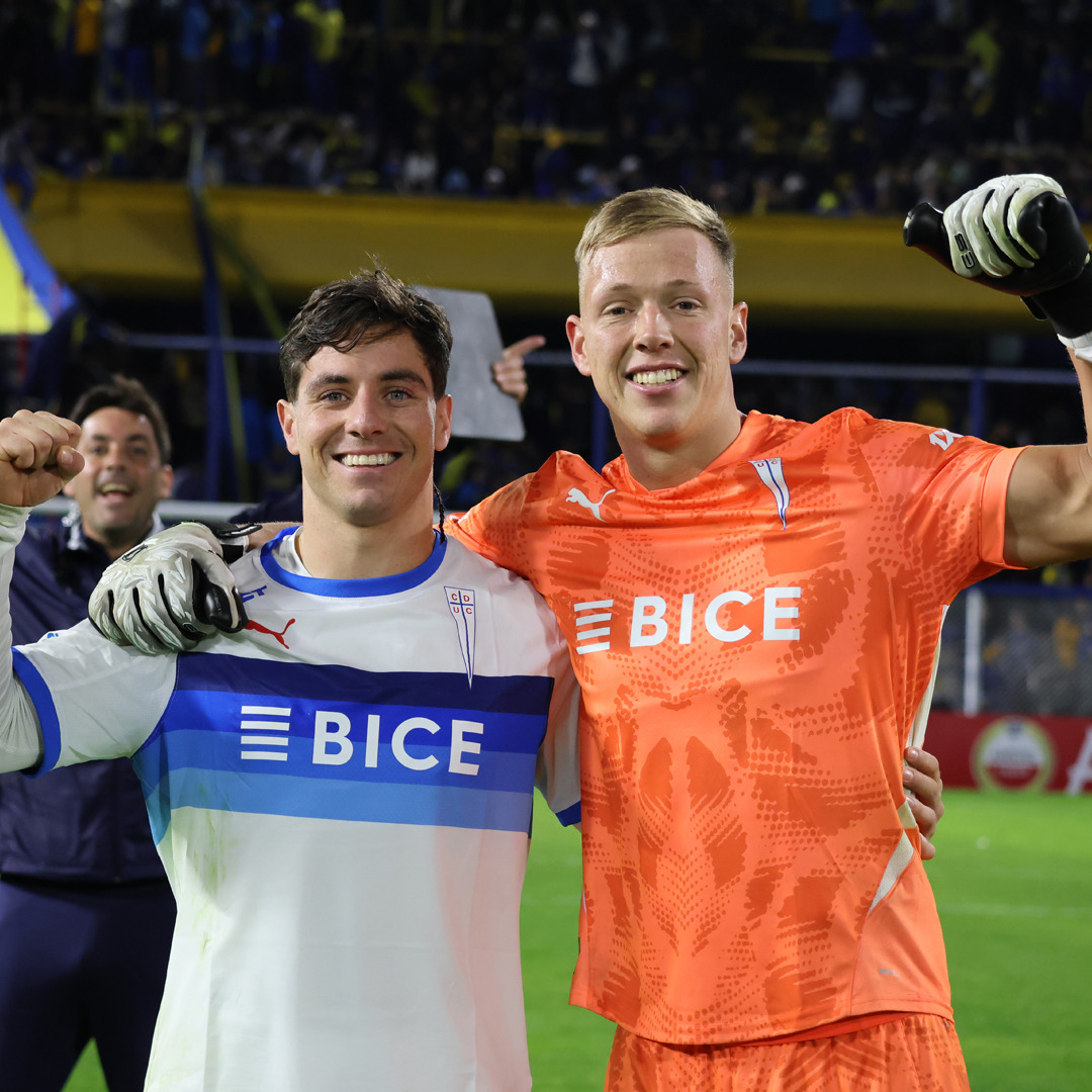 Two smiling soccer players in team jerseys posing together at a stadium